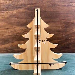 May include: A wooden Christmas tree decoration, 17.78 cm wide and 19.05 cm tall. The tree is made of light-coloured wood and has a simple, classic design, perfect for holiday decor.