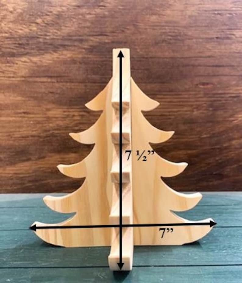 May include: A wooden Christmas tree decoration, 17.78 cm wide and 19.05 cm tall. The tree is made of light-coloured wood and has a simple, classic design, perfect for holiday decor.