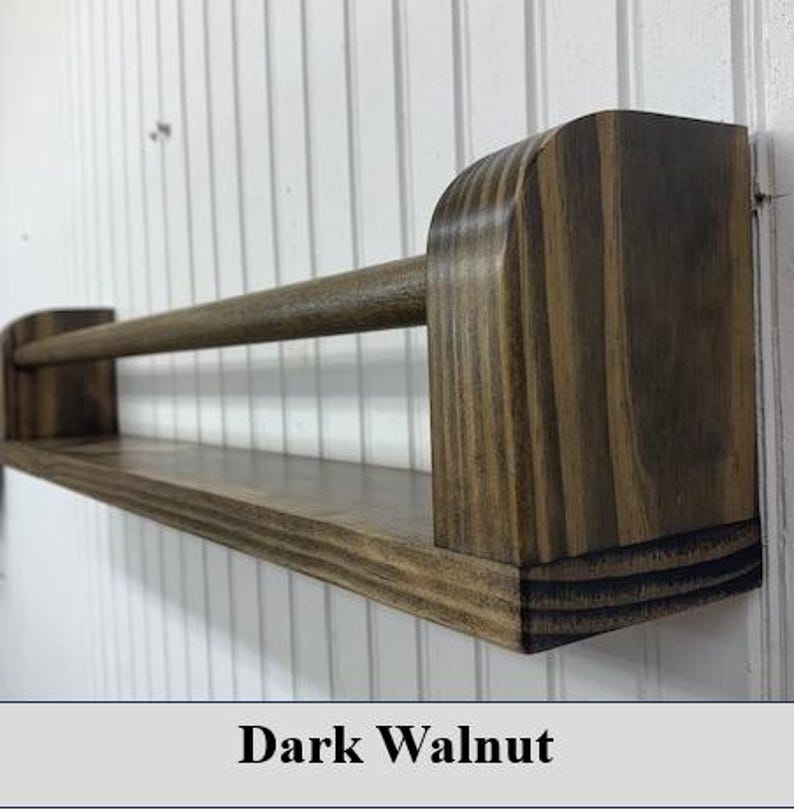 May include: A dark walnut-stained wooden shelf with a rod. The shelf has a rectangular base and rounded end supports. The rod is positioned above the shelf, and the text "Dark Walnut" is at the bottom.