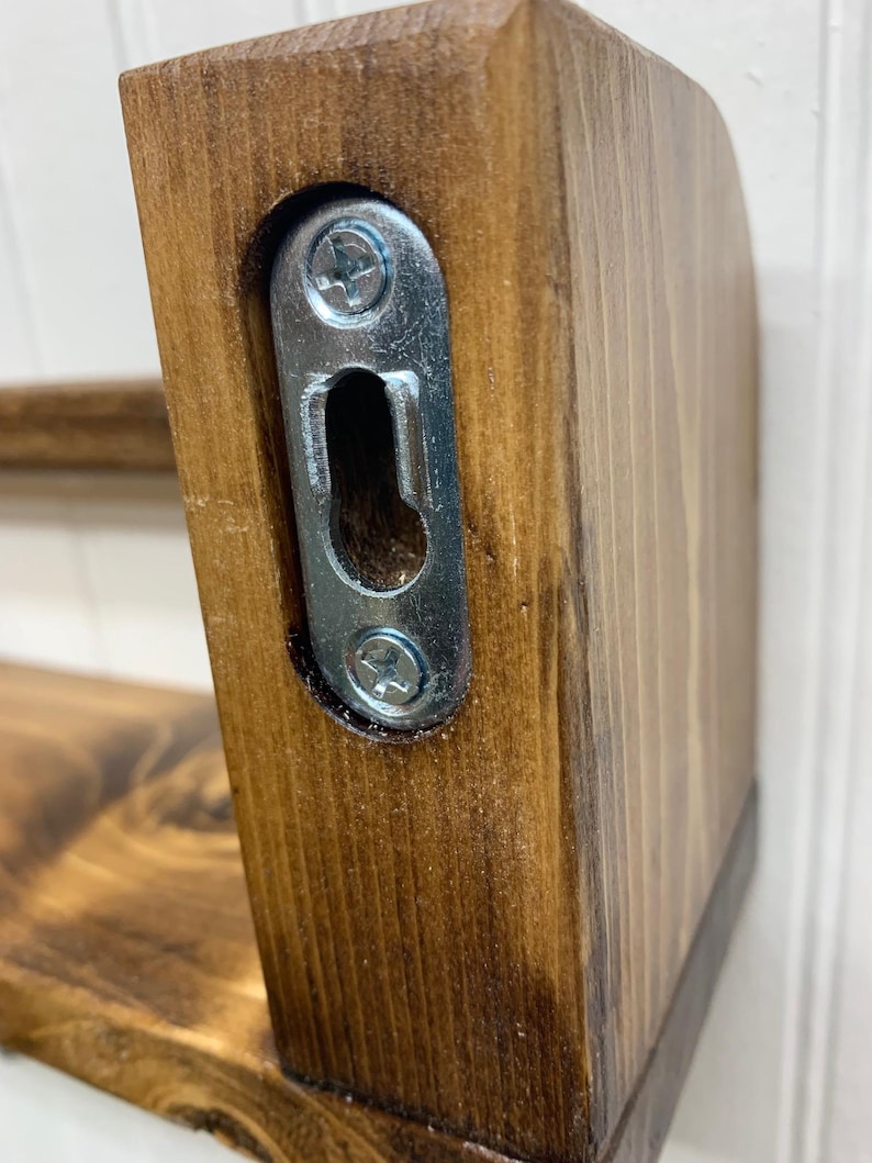 May include: Close-up of a stained wooden shelf with a metal bracket for wall mounting. The wood has a rich, dark brown finish. The bracket is silver and secured with screws, designed for easy installation.