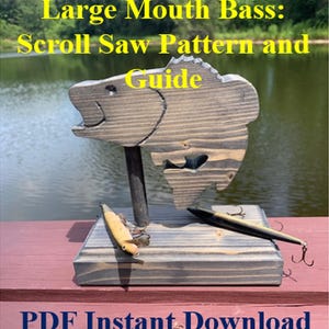 Puede incluir: Un patrón de sierra de calar de madera y una guía para un róbalo. El pez de madera está montado sobre una base de madera con dos señuelos de pesca. El texto "Large Mouth Bass: Scroll Saw Pattern and Guide" es visible.