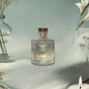 May include: A clear glass bottle with a gold lid and a label that reads "LIWUMI" and "SERENITY" with a white background. The bottle is filled with a clear liquid and is sitting on a white surface.