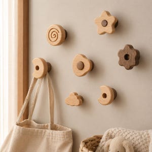 May include: A collection of seven wall-mounted wooden hooks in various shapes including a spiral, star, flower, cloud, and crescent moon. The hooks are crafted from light and dark wood, featuring smooth finishes and circular mounting bases.