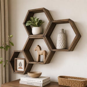 Peut inclure: Un ensemble de quatre étagères murales hexagonales en bois foncé interconnectées. Les étagères contiennent une plante verte dans un pot blanc, un vase beige texturé, une figurine de cheval en bois et un cadre avec une illustration de feuille.
