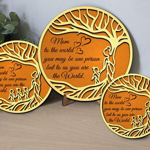 Op de afbeelding: Drie houten plaquettes met een boomontwerp en de tekst "Mam voor de wereld, je bent misschien maar één persoon, maar voor ons ben je de wereld."
