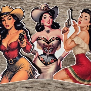 May include: Three die-cut stickers featuring illustrations of women in western-themed attire. One wears a red shirt and tan skirt with two revolvers, another a fringed corset and hat, and the third a white top and red skirt holding a revolver.