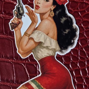 Op de afbeelding: Een vintage-stijl illustratie van een vrouw die een revolver vasthoudt en een kus blaast. Ze draagt een witte off-the-shoulder top, een rode rok met een groen-witte rand en een rode roos in haar zwarte haar. Gouden oorbellen en armbanden maken de look compleet.