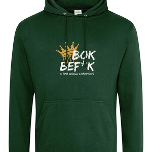 以下が含まれることがあります： 王冠と「Bok Befk 4 Time World Champions」の文字が白で描かれた、濃い緑色のフード付きスウェットシャツです。