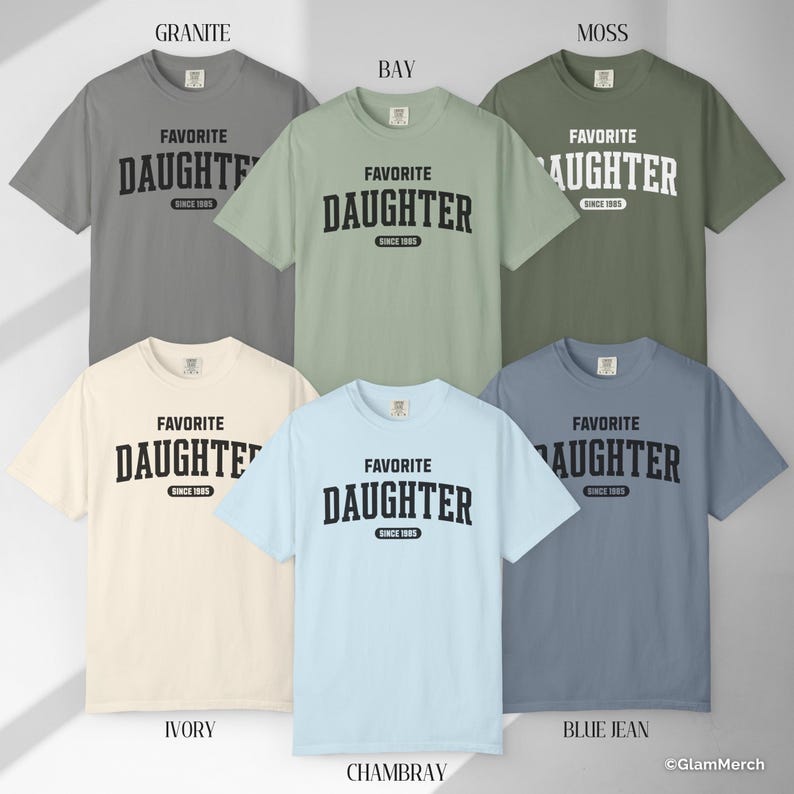 May include: Six short-sleeved t-shirts in various colors: granite, bay, moss, ivory, chambray, and blue jean. Each shirt has the text "FAVORITE DAUGHTER SINCE 1985" printed in black. The shirts are displayed on a neutral background.