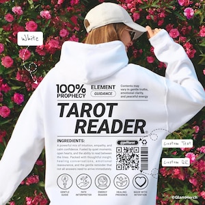 May include: White hoodie with the text "TAROT READER" in bold black letters. The hoodie also features the words "100% PROPHECY" and "ELEMENT GUIDANCE". Additional text includes "INGREDIENTS" and a list of ingredients. A QR code and social media handle are also visible.