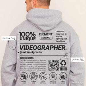 May include: A light grey hoodie with the text "100% UNIQUE VIDEOGRAPHER" and a list of ingredients. The hoodie features a QR code, icons, and the text "@michaelgracier". The back of the hoodie also has the text "ELEMENT EDITING".