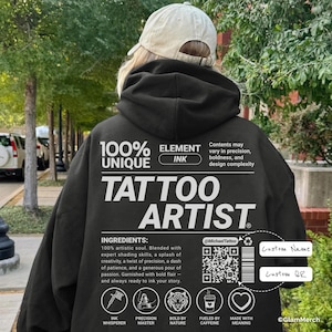 May include: Black hoodie with white text reading "100% UNIQUE ELEMENT INK TATTOO ARTIST." The hoodie features a list of ingredients and a QR code. The design also includes icons and the text "Custom Name" and "Custom QR."