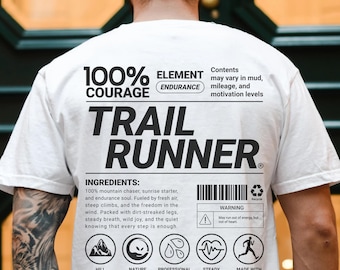 May include: White t-shirt with the text "TRAIL RUNNER" in large black letters. The shirt also features the text "100% COURAGE" and "ELEMENT ENDURANCE". Below the text are ingredient and warning labels with icons.