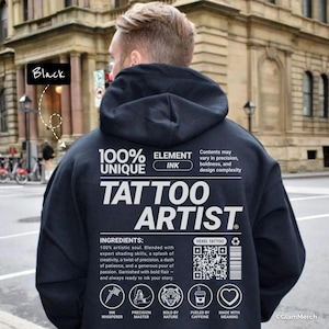 Op de afbeelding: Zwarte hoodie met de witte tekst "TATTOO ARTIST". De achterkant van de hoodie toont ook tekst waaronder "100% UNIQUE ELEMENT INK" en ingrediënten. De hoodie heeft een capuchon en wordt door een persoon gedragen.