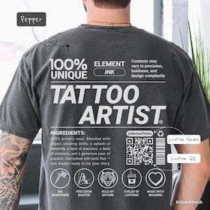 Puede incluir: Camiseta gris oscuro con las palabras "TATTOO ARTIST" en letras blancas grandes. La camiseta también presenta el texto "100% UNIQUE INK" y una lista de ingredientes. También se ve un código QR y el texto "@MichaelTattoo".