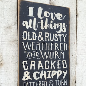 May include: A rectangular wooden sign with a black background and white lettering. The text reads "I love all things old & rusty weathered and worn cracked & chippy tattered & torn faded & vintage."