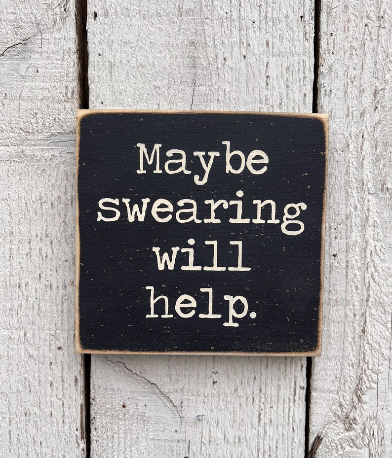 May include: Black wooden sign with white text that reads "Maybe swearing will help."