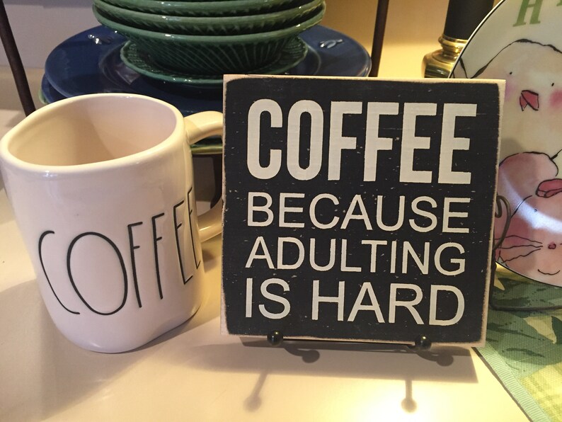 Peut inclure: Une tasse &agrave; caf&eacute; en c&eacute;ramique blanche avec le mot "COFFEE" &eacute;crit en noir sur le c&ocirc;t&eacute;, &agrave; c&ocirc;t&eacute; d'une pancarte en bois noir avec le texte "COFFEE BECAUSE ADULTING IS HARD".