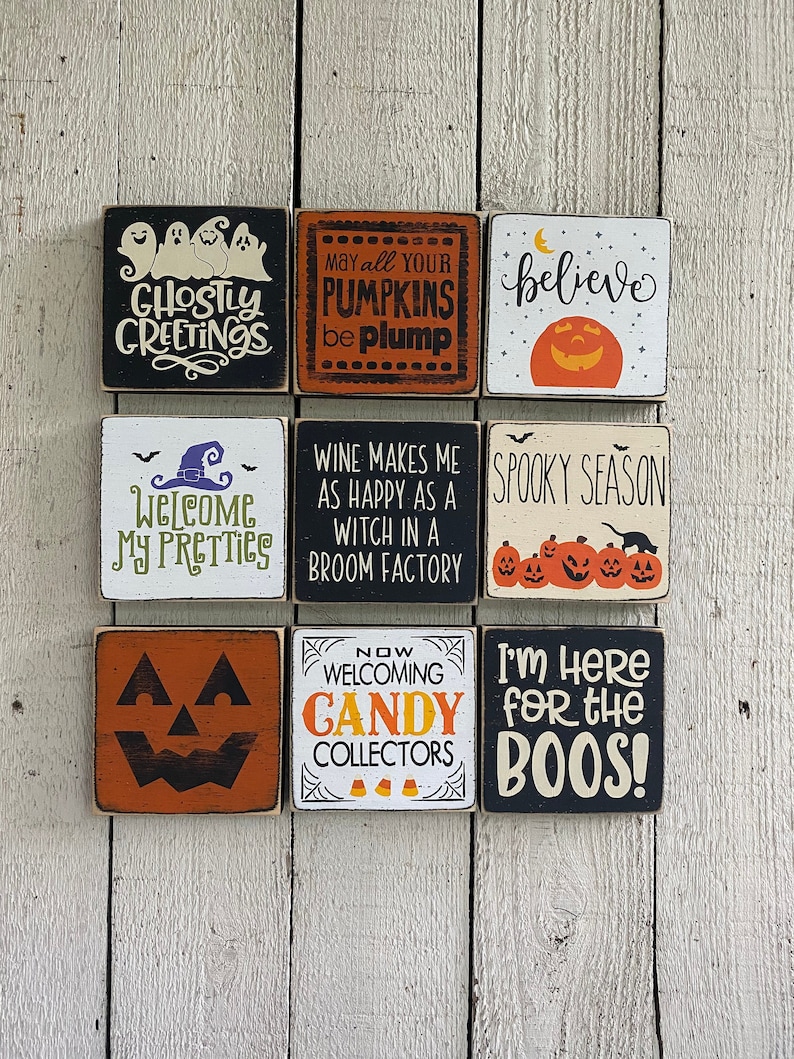 May include: Nine square wooden Halloween signs with various phrases and images. The signs feature phrases like "Ghostly Greetings," "May all your pumpkins be plump," and "I'm here for the boos!" The signs are painted in black, orange, white, and green.