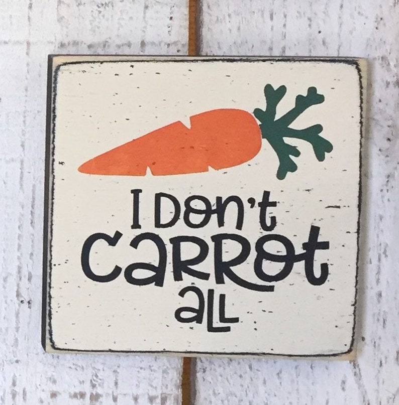 May include: A white wooden sign with a hand-painted orange carrot and green leaves. The sign says "I don't carrot all" in black lettering.