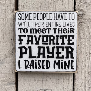 May include: White wooden sign with black text that reads "Some people have to wait their entire lives to meet their favorite player. I raised mine."