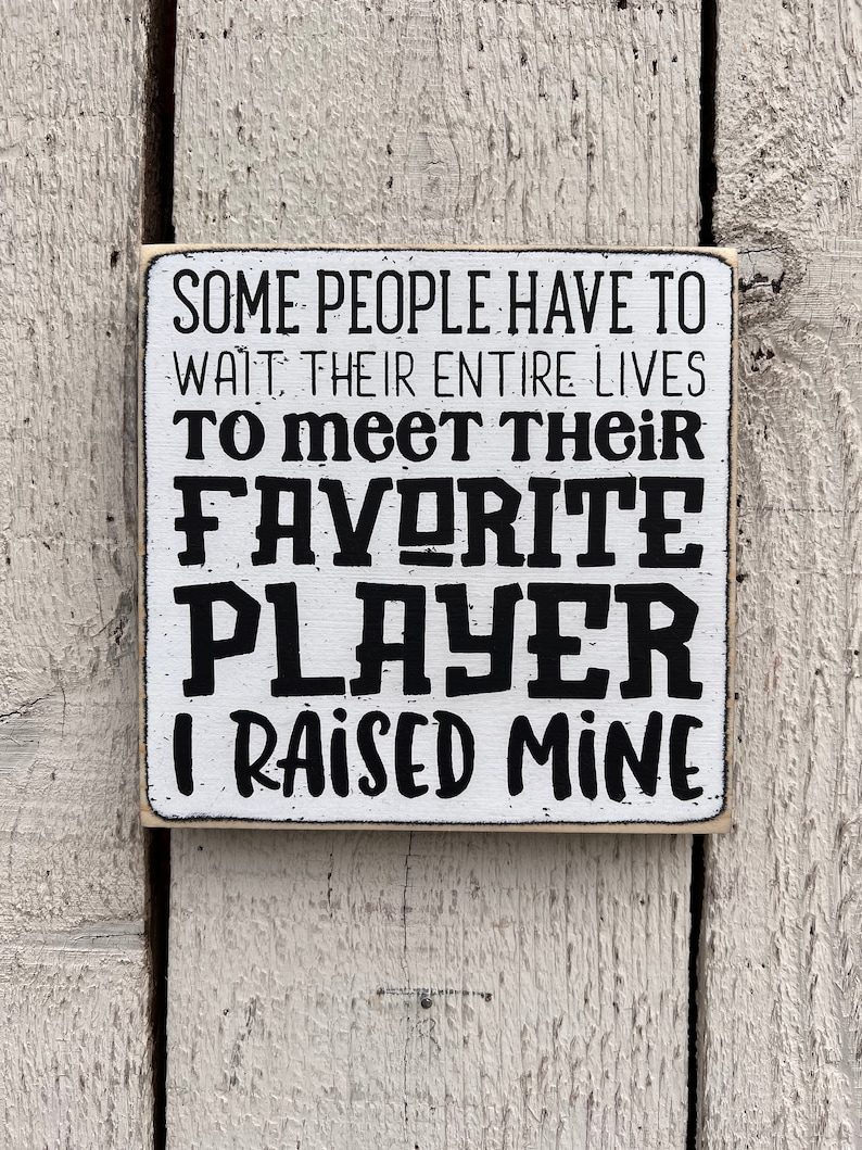 May include: White wooden sign with black text that reads "Some people have to wait their entire lives to meet their favorite player. I raised mine."