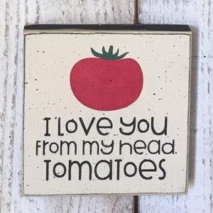 May include: A white wooden sign with black lettering and a red tomato illustration. The sign reads "I love you from my head tomatoes."