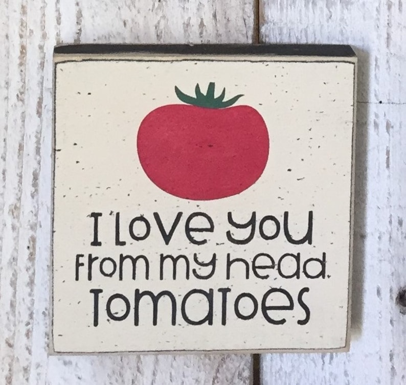 May include: A white wooden sign with black lettering and a red tomato illustration. The sign reads "I love you from my head tomatoes."