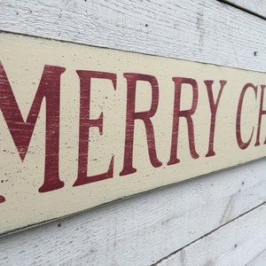 May include: A wooden sign with a distressed white background and red lettering that reads "Merry Christmas".