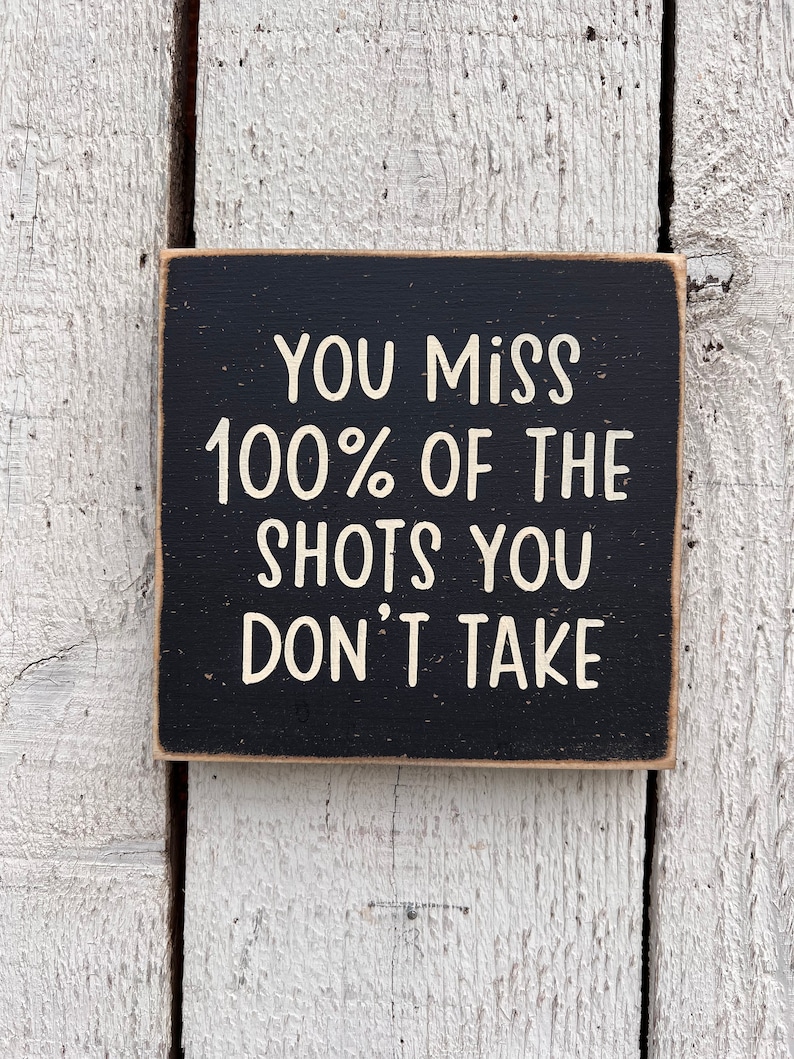May include: Black wooden sign with white text that reads "You miss 100% of the shots you don't take."