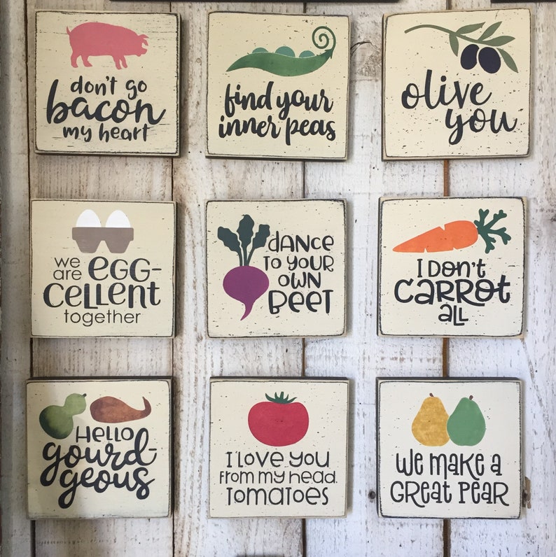 May include: Nine wooden signs with various vegetable puns. The signs are painted in a rustic style with white backgrounds and black lettering. The signs feature puns such as "don't go bacon my heart", "find your inner peas", "we are egg-cellent together", "dance to your own beet", "I don't carrot all", "hello gourd-geous", "I love you from my head, tomatoes", and "we make a great pear".