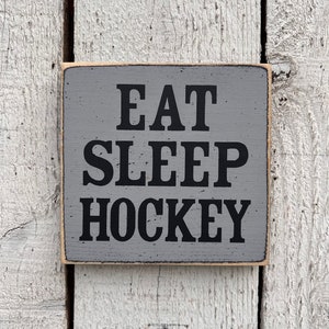 May include: A gray wooden sign with black text that reads "Eat Sleep Hockey".