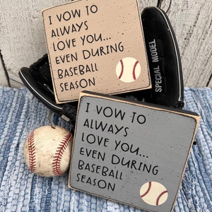 Op de afbeelding: Twee houten borden met de tekst "Ik zweer je altijd lief te hebben... zelfs tijdens het honkbal seizoen" en een honkbal afbeelding. De borden zijn beige en grijs geverfd.
