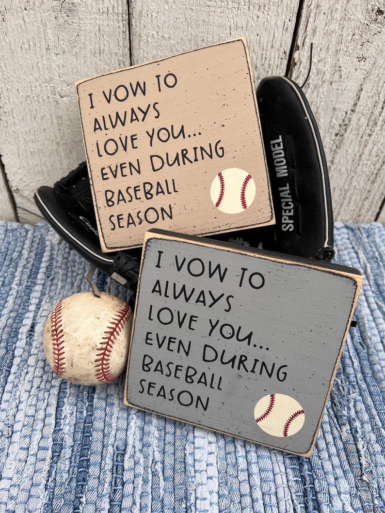 Op de afbeelding: Twee houten borden met de tekst "Ik zweer je altijd lief te hebben... zelfs tijdens het honkbal seizoen" en een honkbal afbeelding. De borden zijn beige en grijs geverfd.
