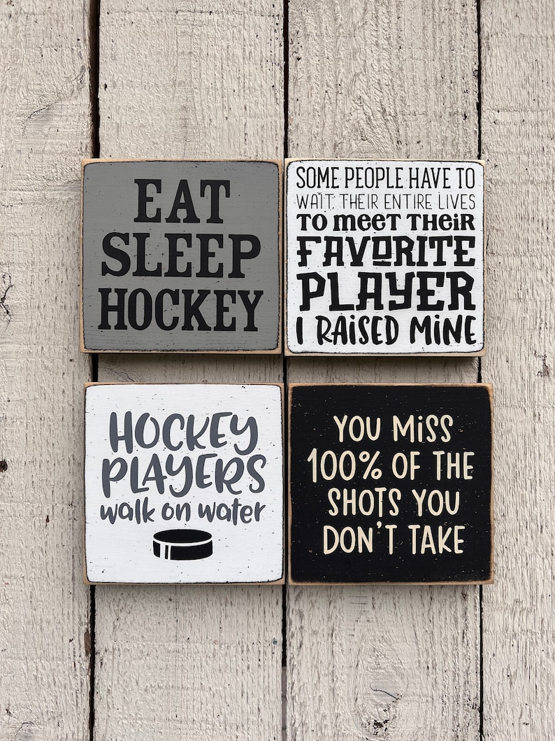 May include: Four wooden signs with hockey-themed sayings. The signs are painted in black, white, and gray. The text on the signs reads: "Eat Sleep Hockey", "Some people have to wait their entire lives to meet their favorite player. I raised mine", "Hockey players walk on water", and "You miss 100% of the shots you don't take".