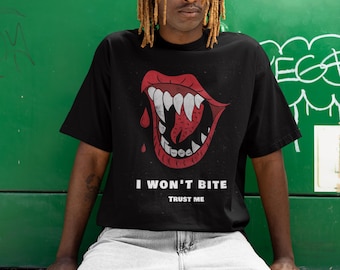May include: Black t-shirt featuring a red and white graphic of a mouth with sharp teeth and a dripping drop of blood. The text "I WON'T BITE" and "TRUST ME" are printed below the graphic. The shirt is worn by a person.