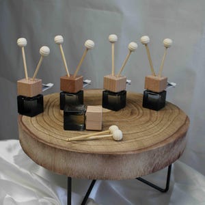 Könnte beinhalten: Ein Set aus sieben kleinen Glasflaschen mit Holzdeckeln und weißen Diffusor-Kugeln. Die Flaschen sind auf einer Holzscheibe mit einem schwarzen Metallständer angeordnet.