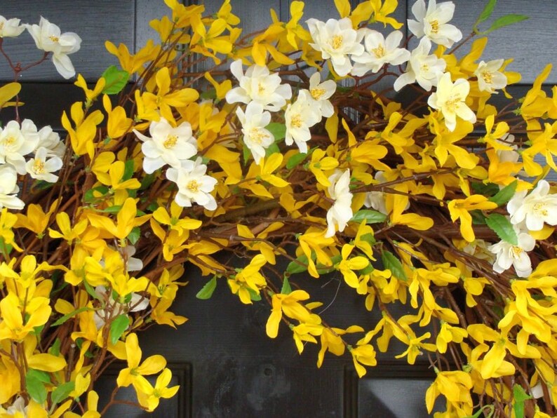 May include: A wreath made of yellow and white flowers. The wreath is made of artificial flowers and is perfect for spring or summer decor.
