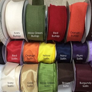 May include: A variety of ribbon spools in different colors and textures, including burlap and satin. The colors include natural, ivory, moss green, red, orange, brown, black, yellow, navy, plum, lavender, white, gold, burgundy, and light pink.