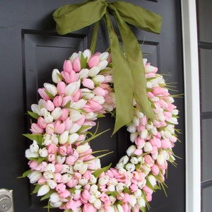 May include: A 24 inch wreath made of pink and white tulips with a green ribbon bow. The wreath is hanging on a black door.