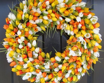 May include: A wreath made of artificial flowers, featuring white, yellow, and orange tulips. The wreath is a circular shape and is suitable for a front door.