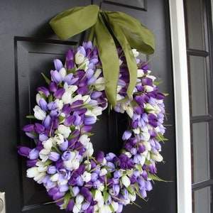 May include: A purple and white tulip wreath with a green ribbon bow. The wreath is hanging on a black door.