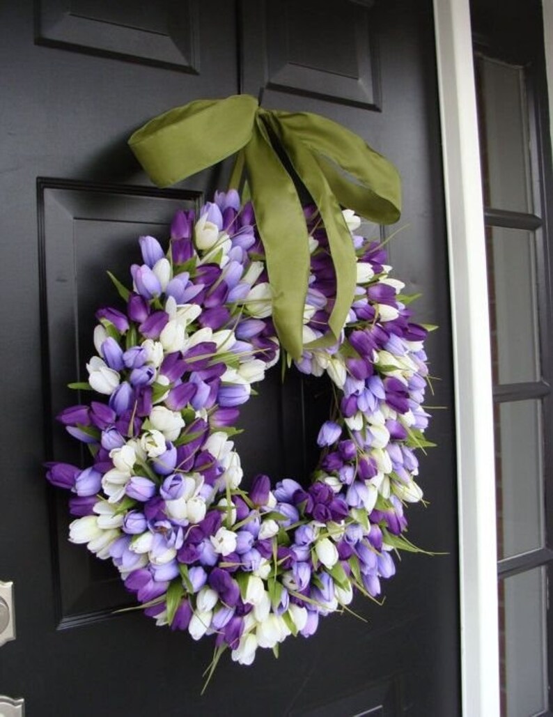 May include: A purple and white tulip wreath with a green ribbon bow. The wreath is hanging on a black door.