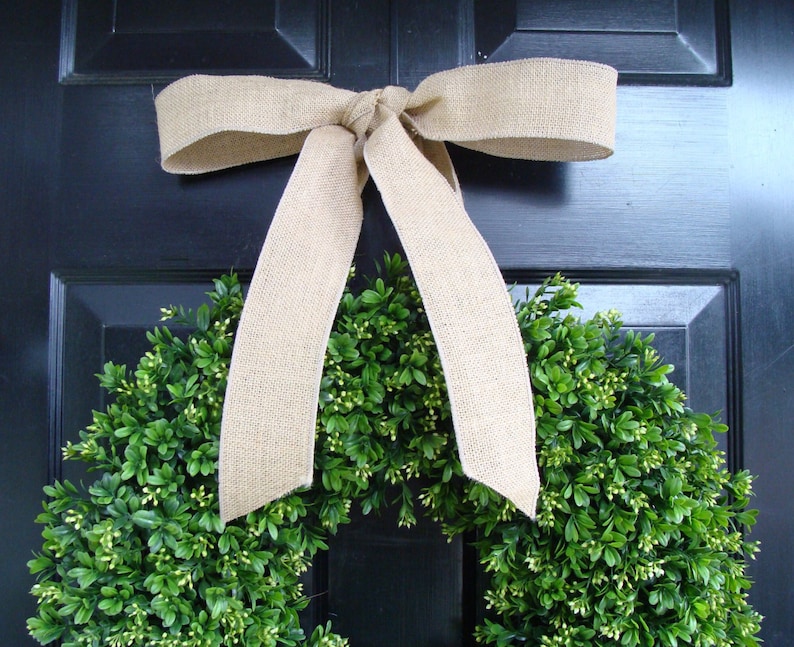 May include: A green boxwood wreath with a burlap bow hanging on a black door.
