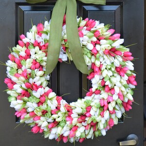 May include: A pink and white tulip wreath with a green bow hanging on a black door.