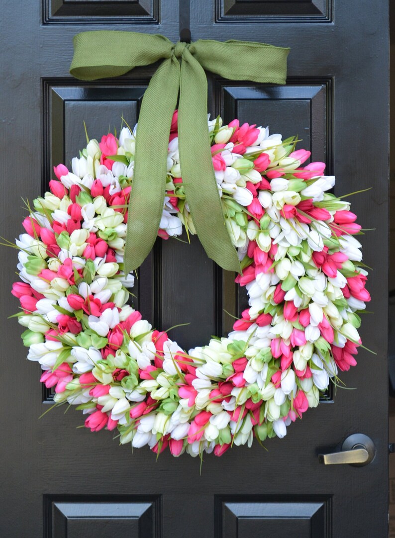 May include: A pink and white tulip wreath with a green bow hanging on a black door.
