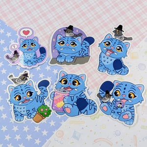 Peut inclure: Une collection de six autocollants représentant un chat bleu de dessin animé avec des rayures de tigre. Chaque autocollant montre le chat dans différentes poses, certains avec un oiseau portant un chapeau. Un chat tient une canette de soda.