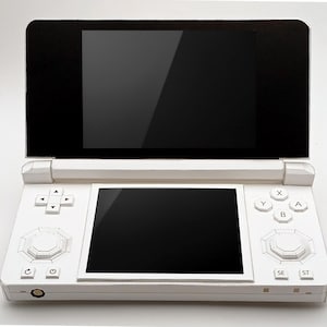May include: A white handheld gaming console with two black screens, one on top and one below. The console has a directional pad, buttons, and a central control. The device is open, revealing the screens.
