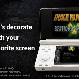 May include: A white Nintendo 3DS handheld game console displaying the "Duke Nukem: Critical Mass" game. The screen shows the game's title and a menu. The text "Let's decorate with your favorite screen" is also visible.