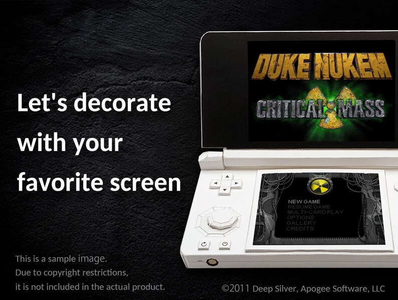 May include: A white Nintendo 3DS handheld game console displaying the "Duke Nukem: Critical Mass" game. The screen shows the game's title and a menu. The text "Let's decorate with your favorite screen" is also visible.